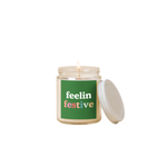 8 oz candle jar with green label on front with text that reads "feelin festive" in white and multi-color letters.