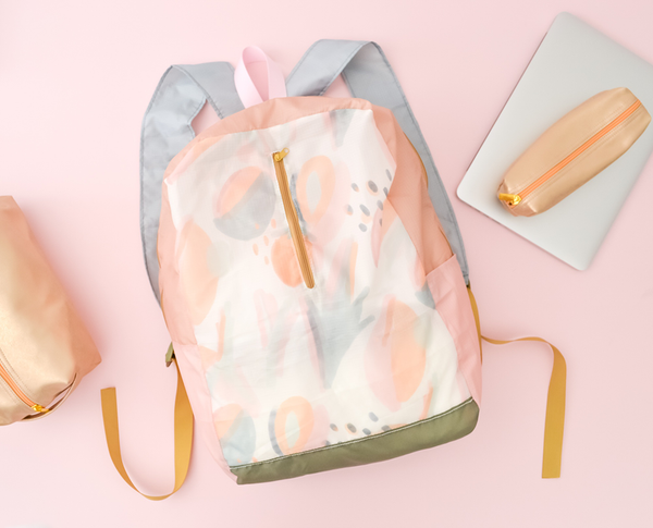 a ripstop backpack with an abstract leaf pattern laying next to a macbook, and two metallic pouches