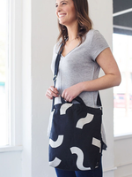 Smiling girl wearing a cute crossbody tote in black canvas with macaroni pattern.