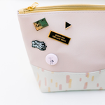 A pink pouch with sunshine pattern sits on a white surface with 5 pins pinned onto the left side of the pouch.