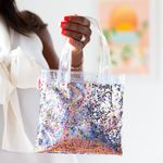 Girl holding tiny handbag in clear vinyl with rainbow glitter confetti.