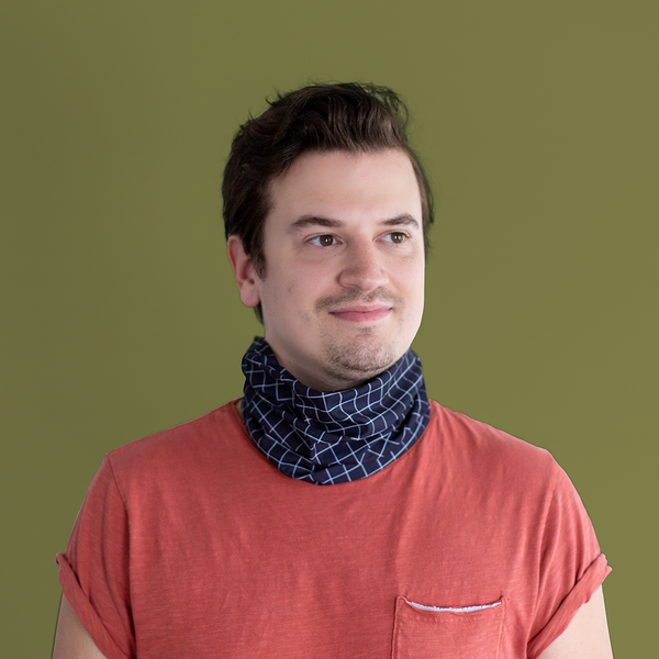 A gridded neck/face cover in black with white grid lines. Cover is displayed on a mans neck, in front of a forrest green background.