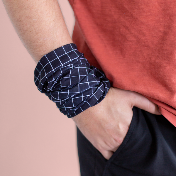 A gridded neck/face cover in black with white grid lines wrapped around a person's wrist.