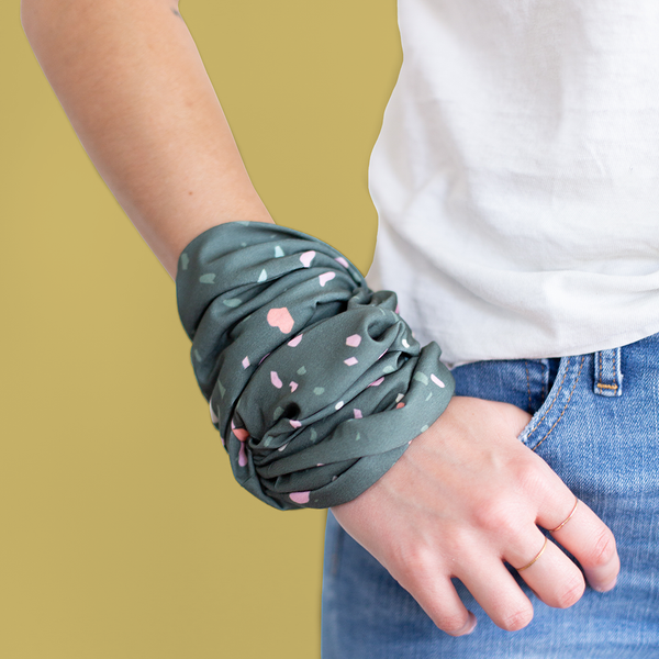 A multicolored terrazzo speckled mask-like item with a dark teal background color. Item is wrapped around someones wrist.