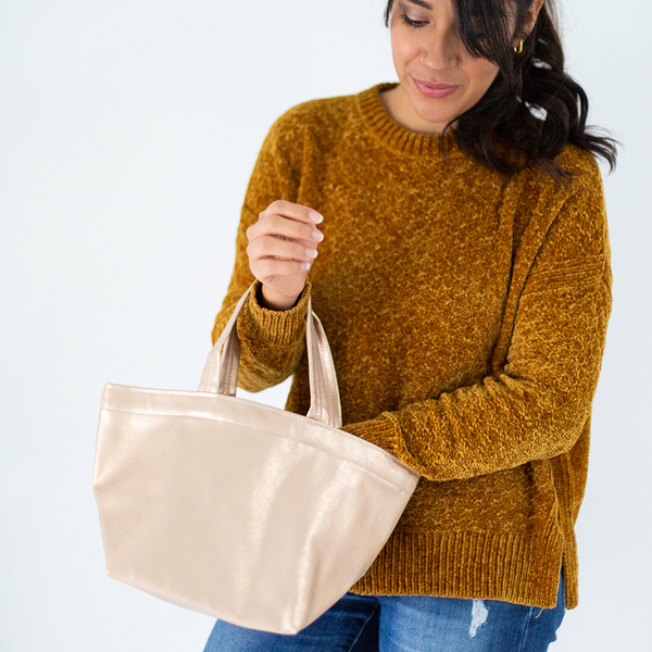 A woman holding a small metallic gold vegan leather tote bag on one arm with her hand in the bag. 