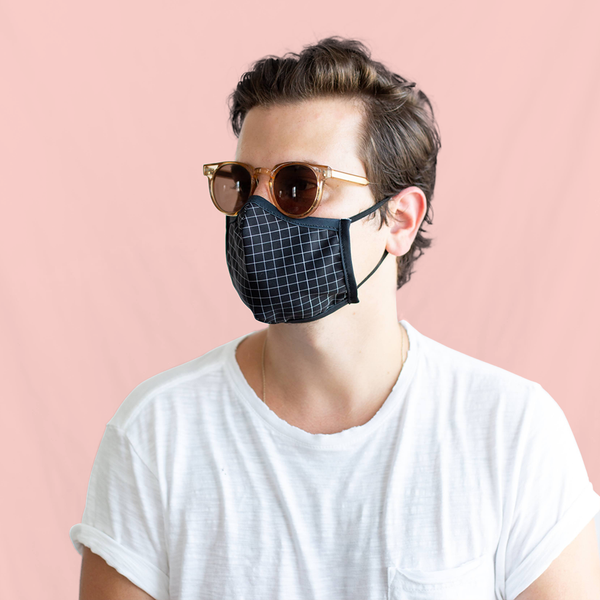 A man wearing a white shirt wears a black and white grid face masks with a pair of sunglasses. 