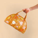 woman holding lil miss sunshine retro print handbag with white, yellow, orange and light pink flowers on an orange background.