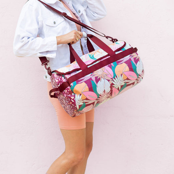 girl with Floral Nights Traveler on her shoulder.The bag has Sangria shoulder and hand straps; with a floral body