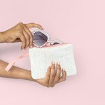 Woman's hands placing rhinestone sunglasses in a natural straw zippered pouch.