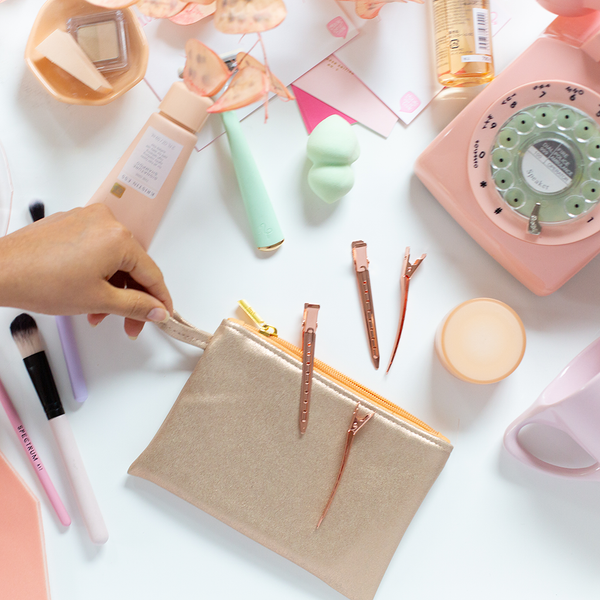 A metallic gold colored rectangular pouch displayed on a white background with cosmetic products such as hair clips, makeup brushes, and an old-fashioned telephone.