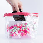 girl putting an iphone into a clear pom pom Tweedle Dee Pom Poms cosmetics bag