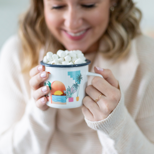 a girl holding a cute white mug with a sunset and plants