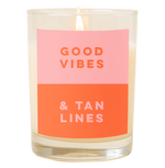  A candle with a decal that says, "Good vibes and tan lines." Top half is a dusty pink color and bottom half of decal is orange.