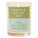 A candle with a decal that says, "Have a great day you fucking badass." The top half is an olive green color and the bottom half of the decal is a dusty blue color.