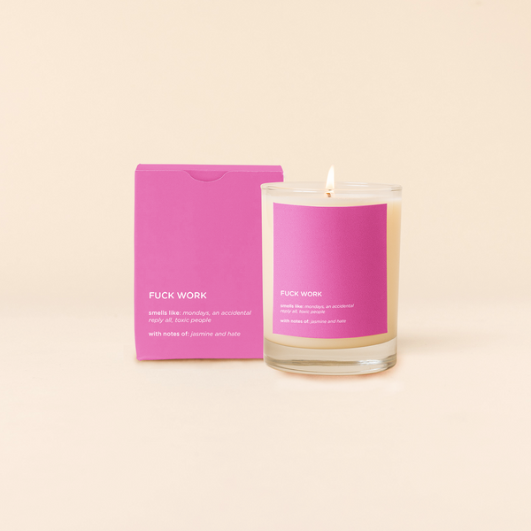 14 oz candle rocks glass with pink decal and text that reads "FUCK WORK, smells like: mondays, an accidental reply all, toxic people, with notes of: jasmine and hate" in white font. Pink box packaging with the same design sits behind the candle.