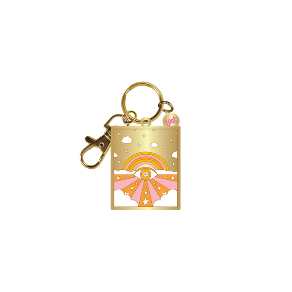 Gold key charm with small white clouds around. Orange, yellow and pink rainbow in the further background. Eye in the center with a white daisy in the middle of the eye. Orange rays with small yellow stars with white clouds in front.