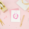 Desk scene with gold desk items and a white greeting card with a hand holding a pink tambourine and the text 