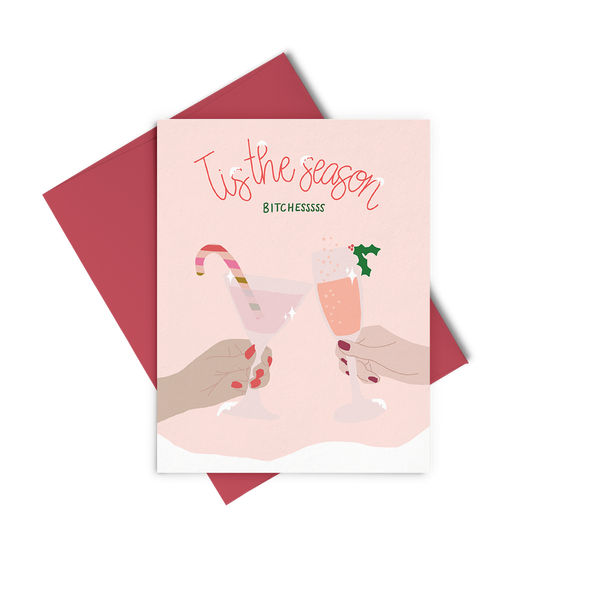 A light pink greeting card with two holiday cocktails clinking and "tis the season bitchessss"