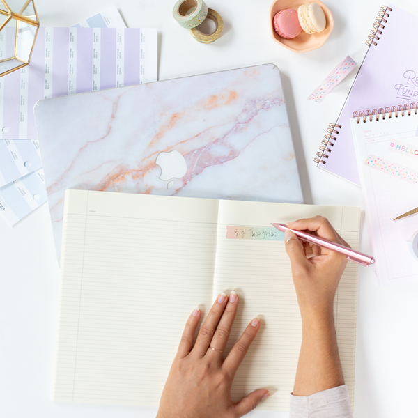 A person writing on a piece of the Meltdown rainbow ombre washi tape. Displayed with a laptop, a Talking out of Turn notebook and task pad, and macaron cookies.