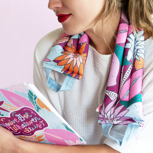 brunette woman with red lipstick resting a floral nights neck wrap on her neck.