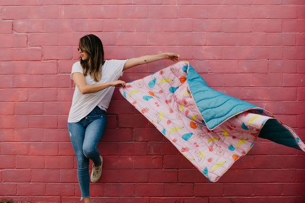 girl holding puffy fruit print blanket blowing in the wind in front of a red brick wall