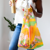 girl holding a medium tote bag geometric scene of rainbow paths and yellow and orange flowers.