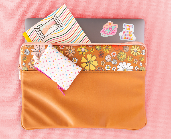 laptop sleeve in brown vegan leather trimmed with fun floral print at the top with peach zipper with laptop, swirled notebook coming out of it with heart print penny pouch on top