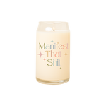 A 16 oz. candle with "Manifest that shit" printed on in multicolored lettering. Twinkle stars are surrounding the phrase.