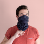 A gridded neck/face cover in black with white grid lines being displayed on a man in front of a dusty pink background.