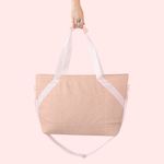 A pink and cream cross stitched tote bag with light pink straps. Bag is being displayed in front of a light pink background.