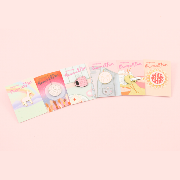 Several of our cute enamel pins on a pink background