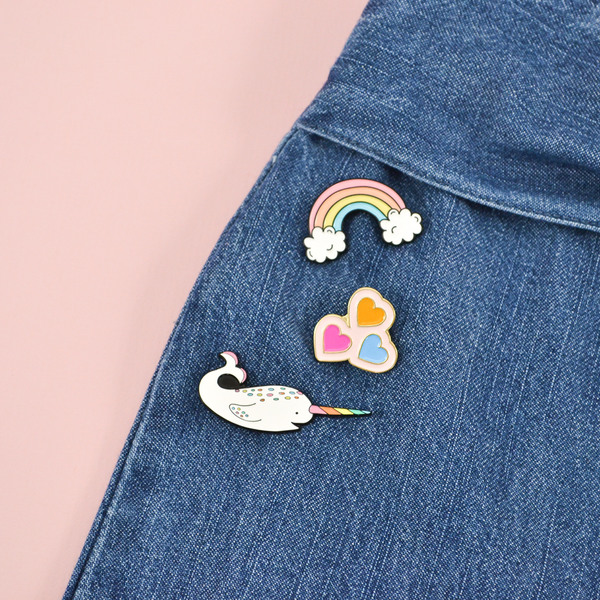 Our rainbow, hearts, and narwhal enamel pins pinned to a denim pair of jeans.