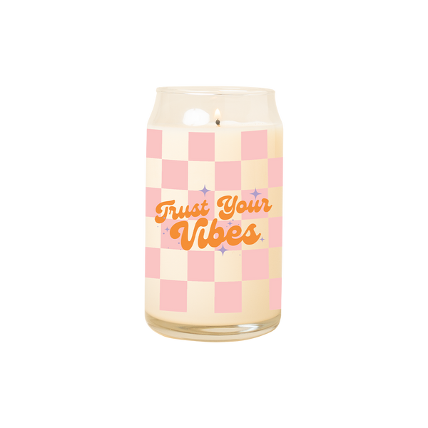 A 16 oz. candle with a pink checkered print design and the phrase "Trust your Vibes" printed on.