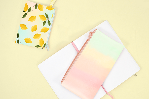 Lemon Sorbet and Daybreak pencil pouches laying on a yellow table with a notebook.