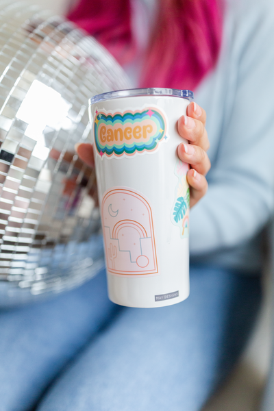 Lady holding a white tumbler with a colorful "cancer" astrology sticker on the side. 