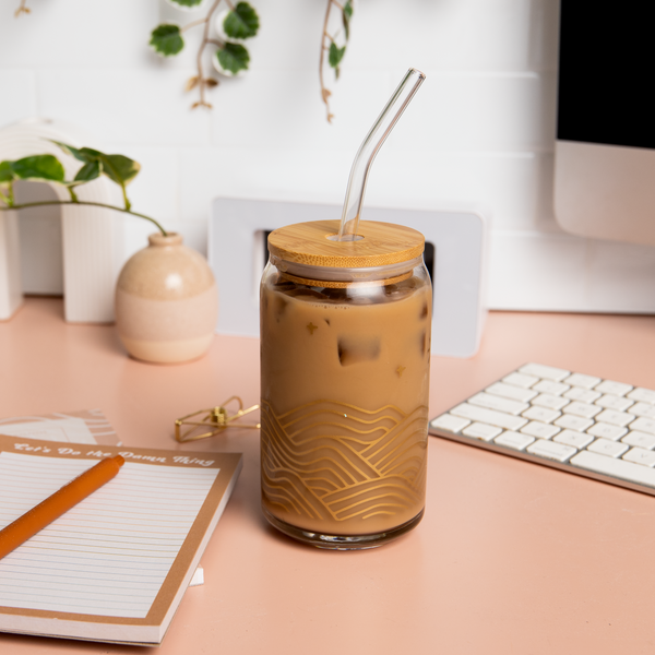 16 oz can glass with lid+straw, "Chill Hills" design in gold wraps around the cup. Cup is filled with iced coffee and surrounded by various stationery supplies.