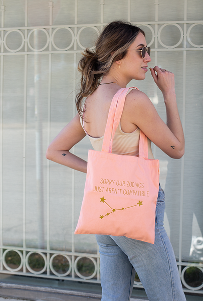 Lady carrying our Peach canvas tote with "SORRY OUR ZODIACS JUST AREN'T COMPATIBLE" in shimmer gold.