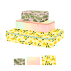 A small, medium, and large sized packing cube. Small cube is a leafy design with a light pink background, middle is a pastel ombre color, and bottom is a lemon design with a light yellow background and green lemon leaves attached to the lemons.