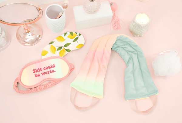 a pastel neck wrap, lemons weighted eye mask, and a pastel sleep mask on a pink background