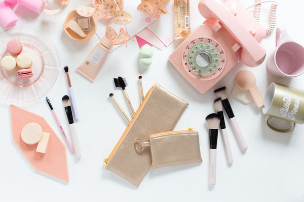 A flat lay image with metallic gold bags used for cosmetic purposes, with make up mugs and make up brushes throughout the scene.