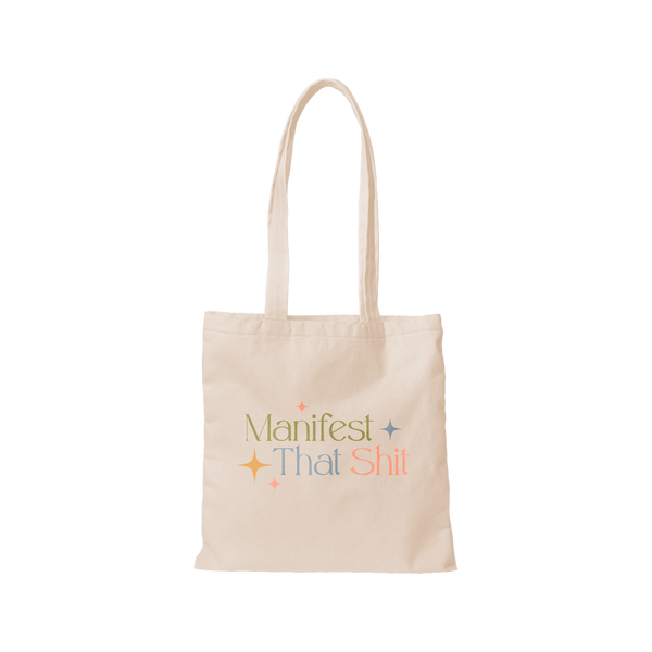 A cream-colored canvas tote bag that says, "Manifest that shit" on the front in different colored lettering. Phrase is surround by minimalistic sparkle stars. 