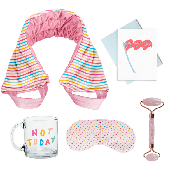 flat image of a collection of self care items including a neck wrap in a rainbow wavy line print, a clear glass mug that says not today, a weighted eye mask with a tiny hearts imprint, a greeting card that yes you can, and a rose quartz roller with roll with it imprinted in dark pink. 