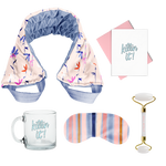 flat image of a collection of self care items including a neck wrap in a small floral print, a clear glass mug that says killing it, a weighted eye mask with blue striped imprint, a greeting card killing it, and a quartz roller with roll with it imprinted in  coral. 