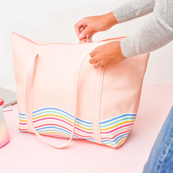 Woman stands in jeans and a sweater unzipping the weekender bag, which is standing up and packed this items.