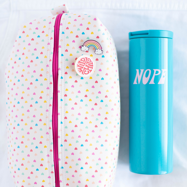 A white, medium-sized pouch with multicolored mini hearts printed all over. Next to the pouch is a bright blue tumbler with the phrase "Nope" printed on in light purple lettering. Both displayed on a white background.