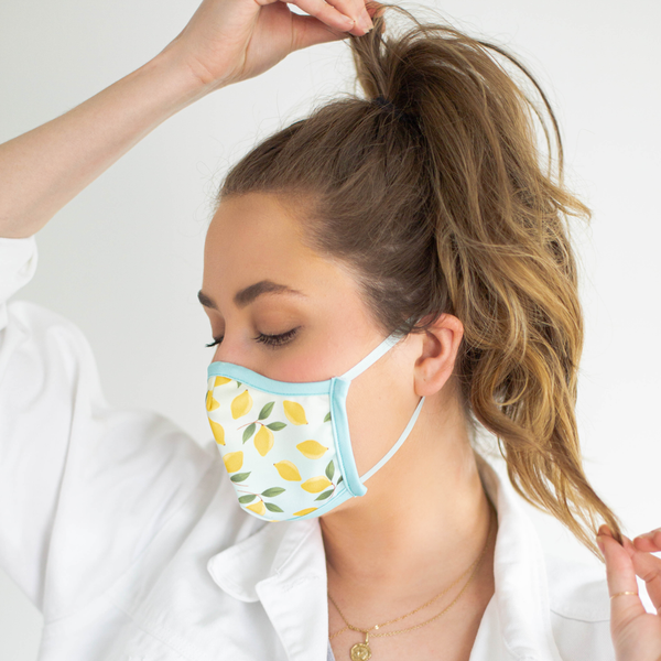 A brunette wears a ombre face mask with lemons illustrated on the mask. 